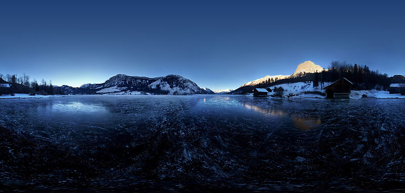Der vereiste Grundlsee in der Dämmerung, im Hintergrund Bergpanorama, teilweise schon mit Sonne bedeckt.