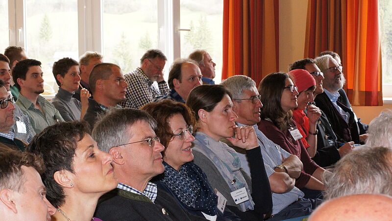 Viele Menschen sitzen in einem Raum nebeneinander und schauen in eine Richtung.